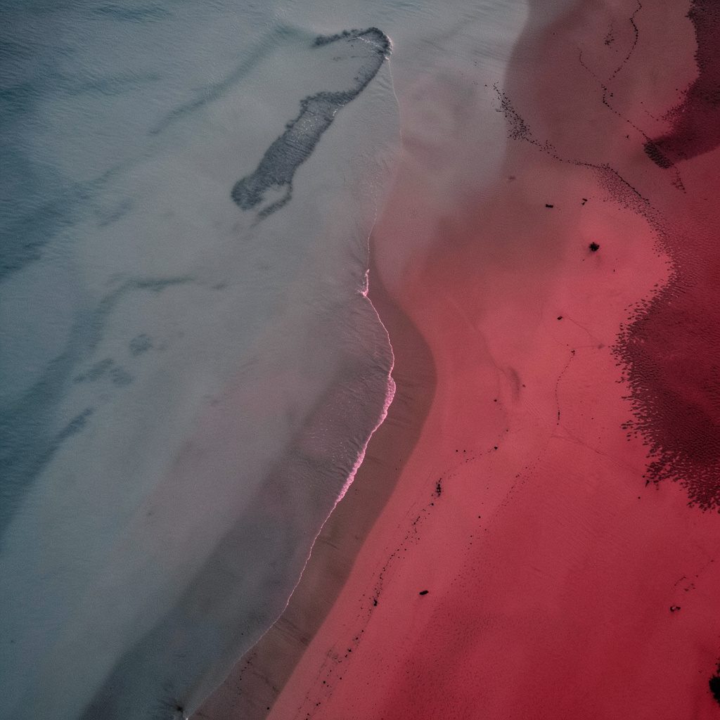 Aerial view of a curving shoreline where muted cool tones meet warm sand, calm abstract mood